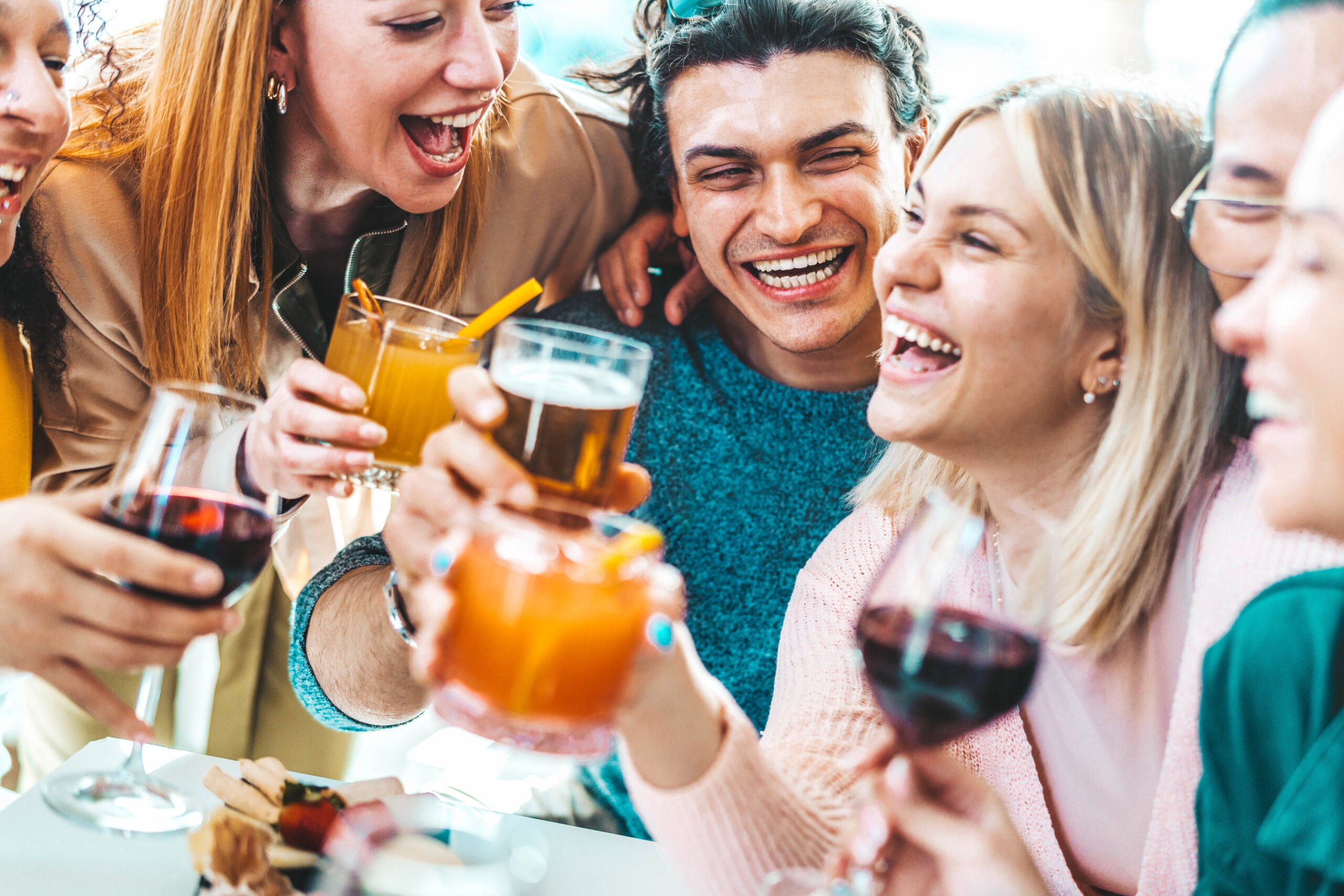 Happy friends enjoying happy hour sitting at bar restaurant table - Young people having fun hanging out on weekend day - Food and beverage concept with guys and girls drinking alcohol together